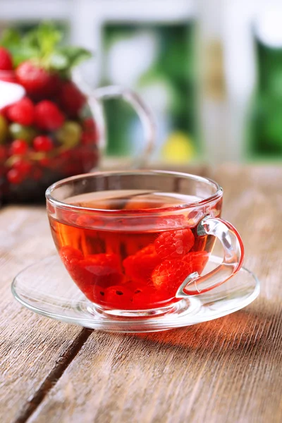 Té rojo de frutas con bayas silvestres en taza de vidrio, sobre mesa de madera, sobre fondo brillante —  Fotos de Stock