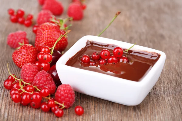 Ripe sweet berries and liquid chocolate on wooden table — Stock Photo, Image