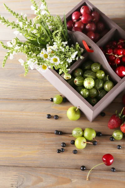 Bayas frescas en caja de madera y flores en la mesa, de cerca — Foto de Stock