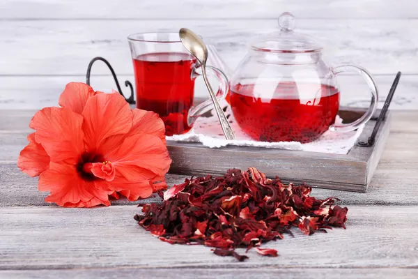 Hibiskus te i glas tekanna och blomma på färg servett på trä bakgrund — Stockfoto