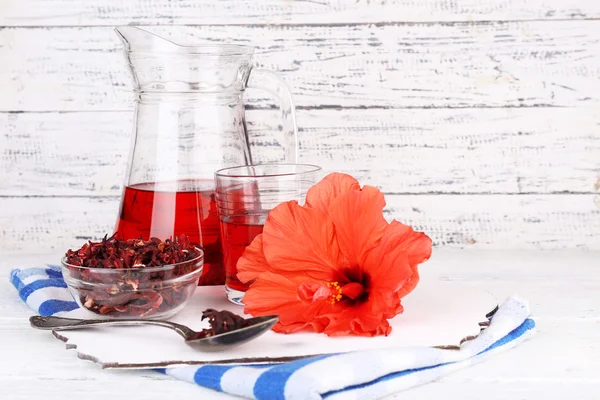 Холодный чай гибискус в стеклянном кувшине с цветком гибискуса на деревянном фоне — стоковое фото