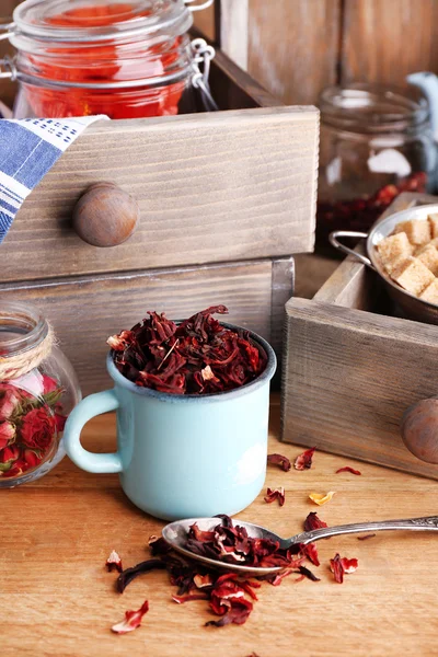 Chá de hibisco seco na caneca a cores, açúcar mascavo na caixa no fundo de madeira — Fotografia de Stock