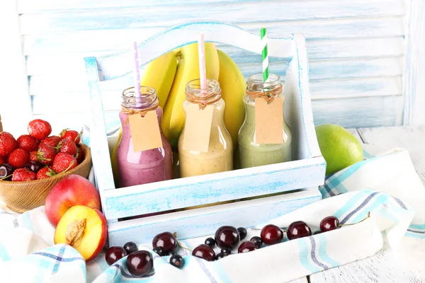 Garrafas de delicioso smoothie em cesta de madeira na mesa, close-up — Fotografia de Stock