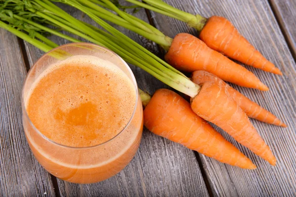 Glas morotsjuice och färska morötter på trä bakgrund — Stockfoto