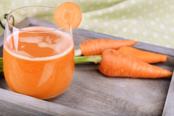 Glass of carrot juice and fresh carrots on wooden tray on table close up — Stock Photo, Image