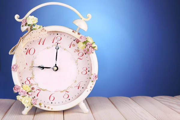 Beautiful vintage alarm clock with flowers on wooden table, on blue background — Stock Photo, Image