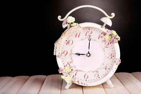 Beautiful vintage alarm clock with flowers on wooden table, on black background — Stock Photo, Image
