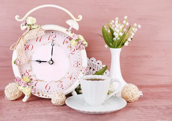 Beautiful vintage alarm clock with flowers and cup of tea on pink wooden background — Stock Photo, Image