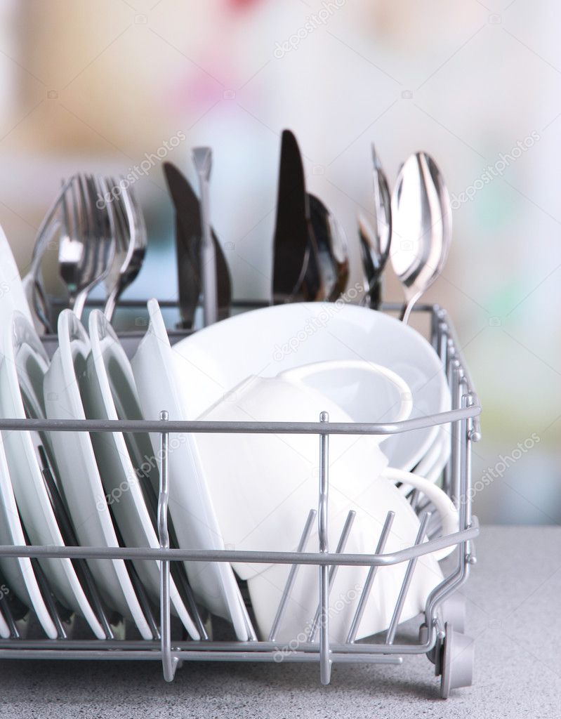 Clean dishes drying on metal dish rack on light background