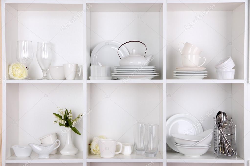 Different white clean dishes on wooden shelves