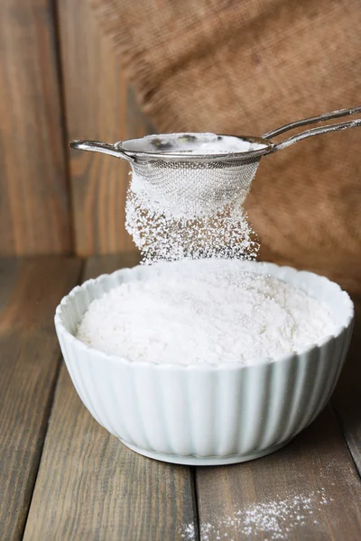 Peneirando farinha em tigela na mesa — Fotografia de Stock