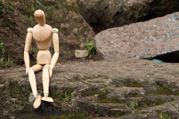 Wooden pose puppet sitting on stone — Stock Photo, Image