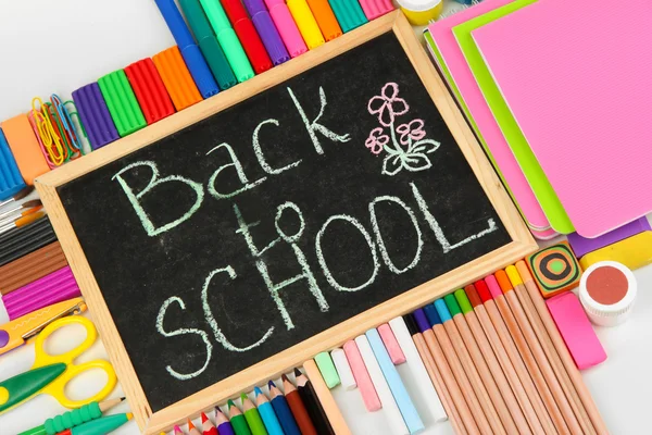 Die Worte "back to school" in Kreide geschrieben auf der kleinen Schulbank mit verschiedenen Schulmaterialien in Großaufnahme — Stockfoto