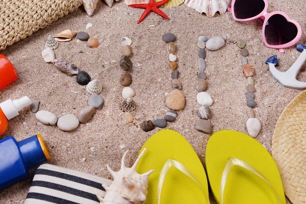 Palabra sol hecha de conchas de mar y piedras sobre arena con accesorios de playa —  Fotos de Stock