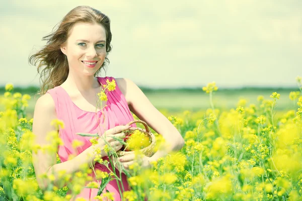 Beautiful young woman holding wicker basket with cherries in field — Stock Photo, Image