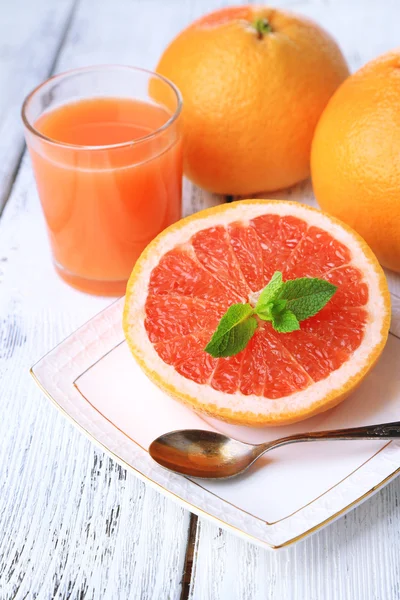 Hälfte Grapefruit, Glas mit frischem Saft und Löffel auf Teller auf hellem Hintergrund — Stockfoto