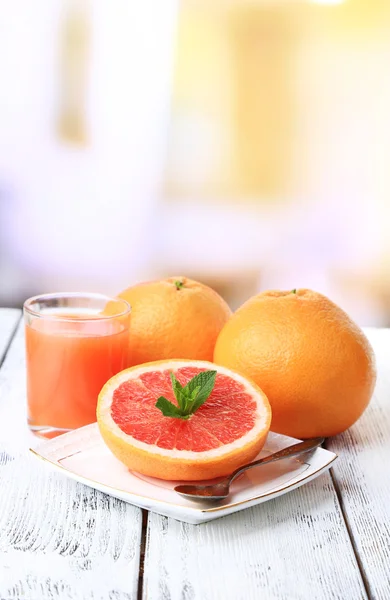 Mezza di pompelmo, bicchiere di succo fresco e cucchiaio su piatto su tavolo di legno, su sfondo luminoso — Foto Stock