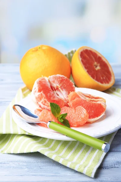 Ripe peeled grapefruits on plate, on color wooden table, on light background — Stock Photo, Image
