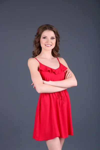 Krásná mladá dívka v červených šatech na šedém pozadí — Stock fotografie