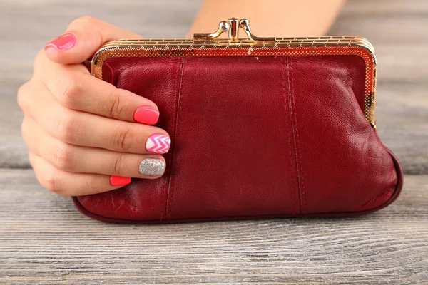 Mano femenina con elegantes uñas de colores sosteniendo pequeña bolsa, sobre fondo de madera — Foto de Stock