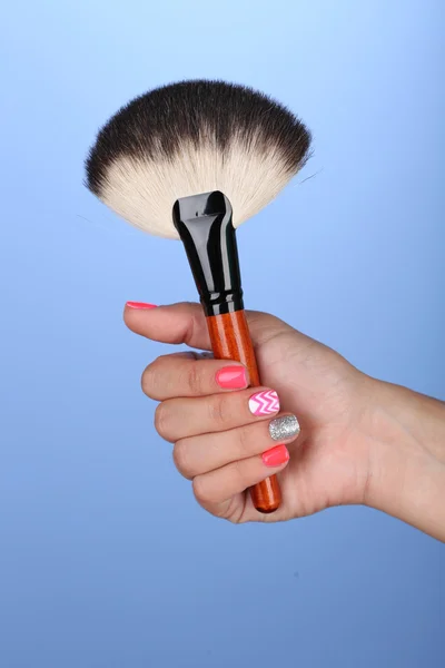 Kvinnlig hand med eleganta färgstarka naglar håller pensel, färg bakgrunden — Stockfoto