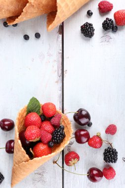 Beyaz ahşap zemin üzerinde şeker koni içinde farklı olgun çilek