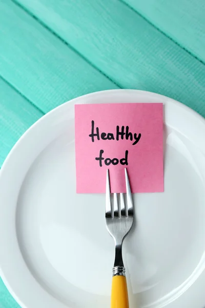 Note paper with message  attached to fork, on plate, on wooden background — Stock Photo, Image