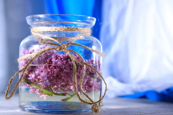 Lindas flores lilás em frasco de vidro, na mesa de madeira cor, no fundo brilhante — Fotografia de Stock