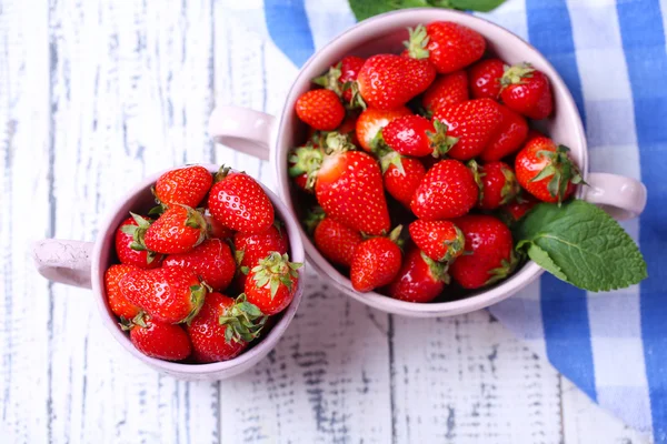 Maturi dolci fragole in pentola e la tazza su sfondo di legno a colori — Foto Stock