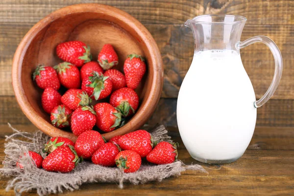 Reife süße Erdbeeren in Holzschale und Krug mit Milch auf farbigem Holzhintergrund — Stockfoto