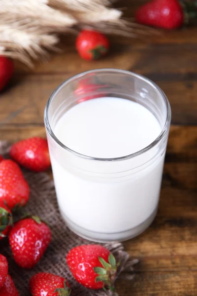 Reife süße Erdbeeren und Glas mit Milch auf farbigem Holzhintergrund — Stockfoto