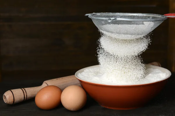 Sifting flour into bowl on table on wooden background — Stock Photo, Image