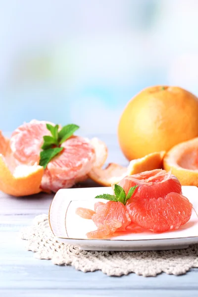 Спелые грейпфруты на тарелке, на цветном деревянном столе, на светлом фоне — стоковое фото