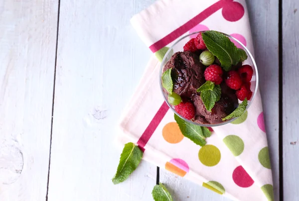 Chocolate ice cream with mint leaf and ripe berries in glass bowl, on color wooden background