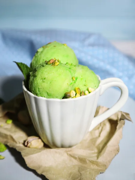 Crème glacée savoureuse à la pistache dans une tasse sur une table en bois, sur fond bleu — Photo