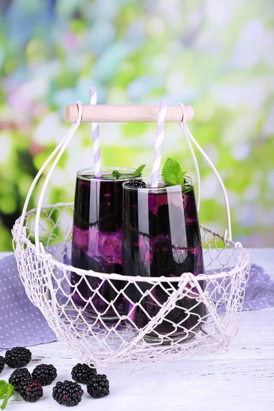 Tasty cool blackberry lemonade with ice on wooden table, on nature background — Stock Photo, Image