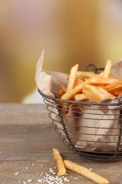 Tasty french fries in metal basket on wooden table, on light background