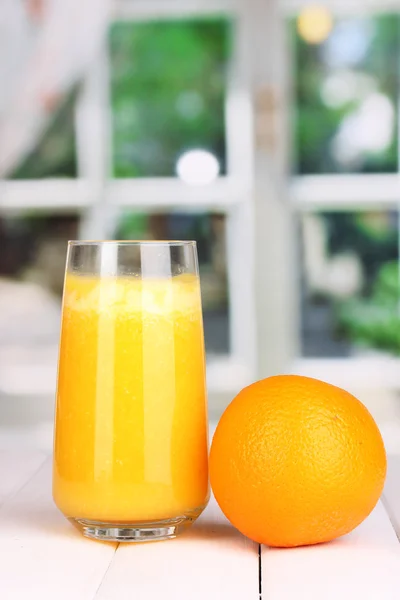 Ποτήρι φρέσκο χυμό πορτοκαλιού σε ξύλινο τραπέζι, σε φόντο παράθυρο — Φωτογραφία Αρχείου