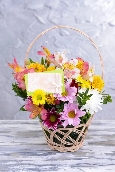 Beautiful bouquet of bright flowers in wicker basket on table on grey background — Stock Photo, Image