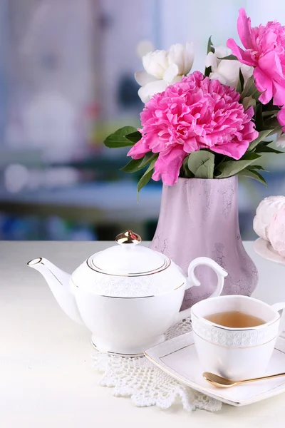 Composición de hermosas peonías en jarrón, té en taza y malvavisco, sobre mesa, sobre fondo claro — Foto de Stock