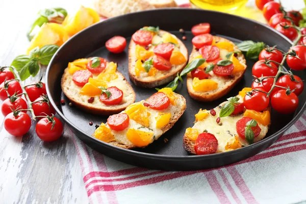 Smakelijke bruschetta met tomaten op pan, op oude houten tafel — Stockfoto