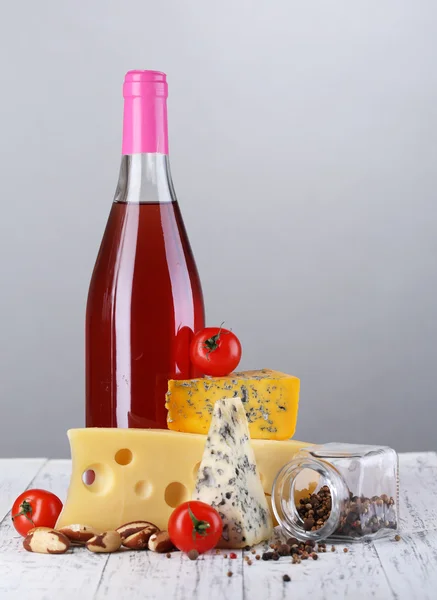 Pink wine and different kinds of cheese on grey background — Stock Photo, Image