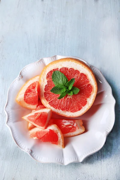 Reife Grapefruits auf Teller auf farbigem Holzhintergrund — Stockfoto