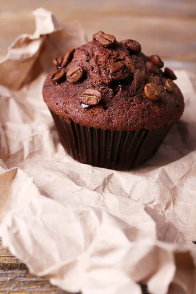 Chocolate muffin and coffee grains on paper, on wooden background — Stock Photo, Image