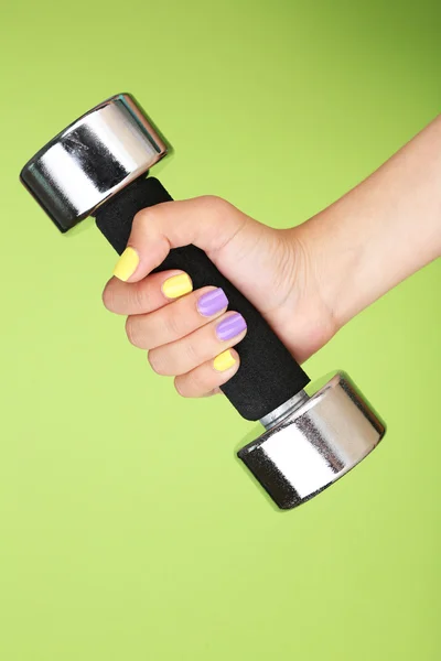 Female hand with stylish colorful nails holding dumbbell, on color background — Stock Photo, Image