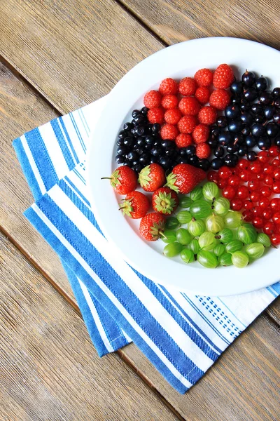 Лесные ягоды на тарелке, на цветном деревянном фоне — стоковое фото