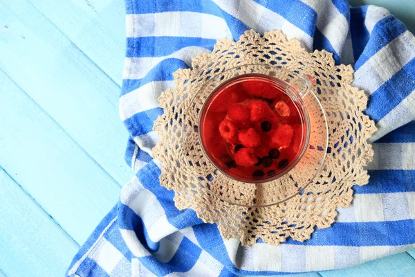 Thé rouge aux fruits avec des baies sauvages dans une tasse en verre, sur fond en bois — Photo