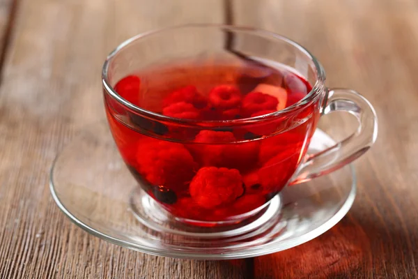 Фруктово-красный чай с лесными ягодами в стеклянной чашке, на деревянном фоне — стоковое фото