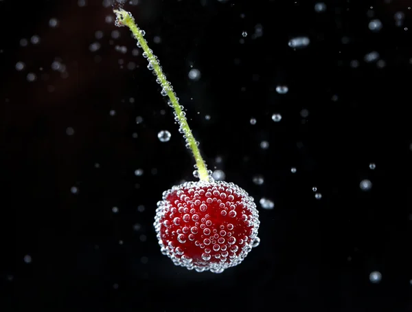 Cereja bonita na água com bolhas, no fundo preto — Fotografia de Stock