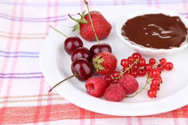 Ripe sweet berries and liquid chocolate on tablecloth — Stock Photo, Image